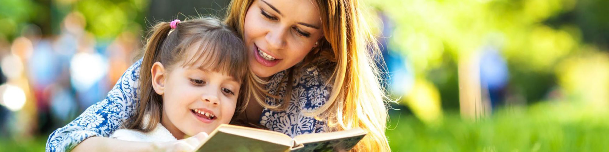 mom and daughter read a book in a field